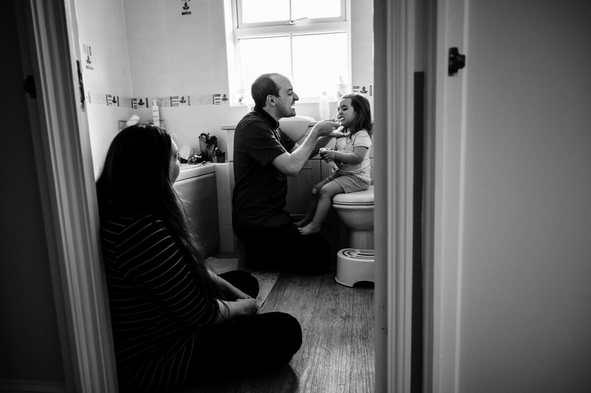 Dad brishing his daughters teeth with mum looking on at home family photoshoot rutland