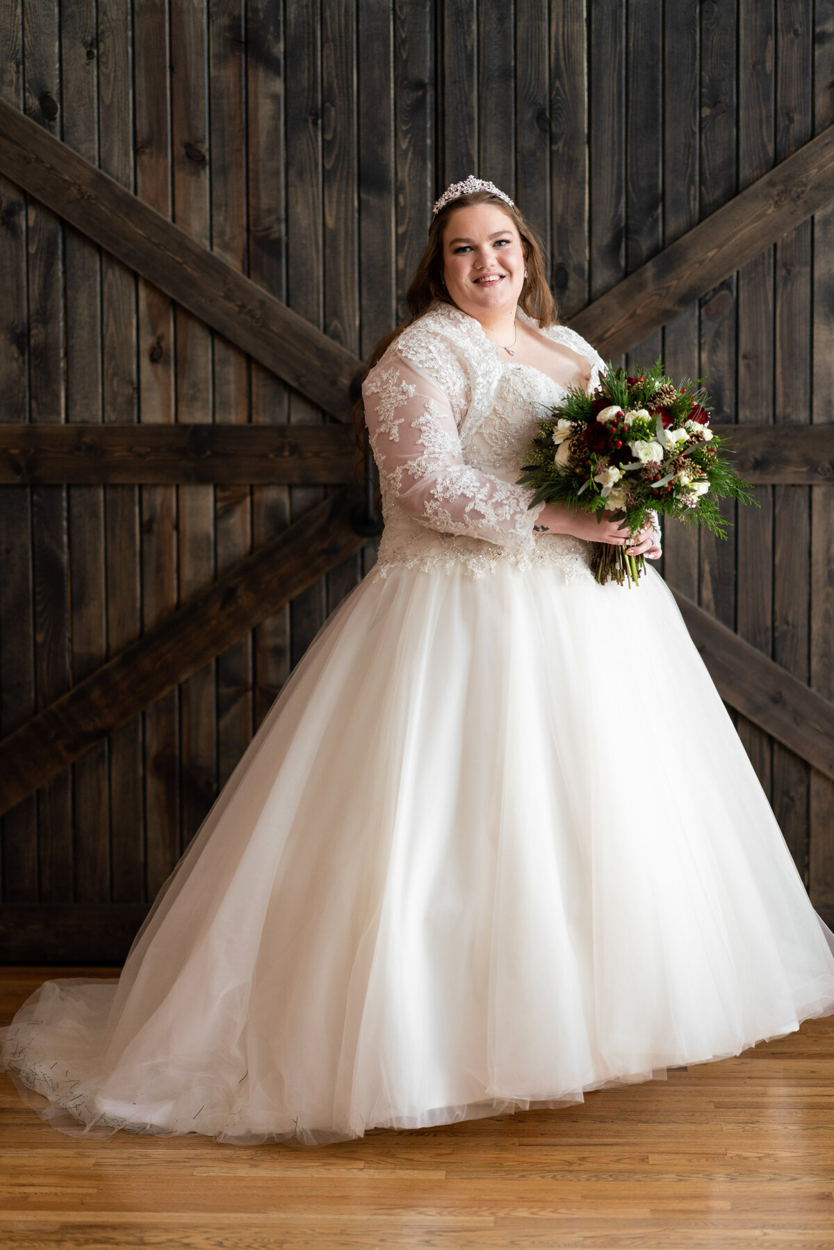 Plus size bride holds flowers and smiles at camera on wedding day.
