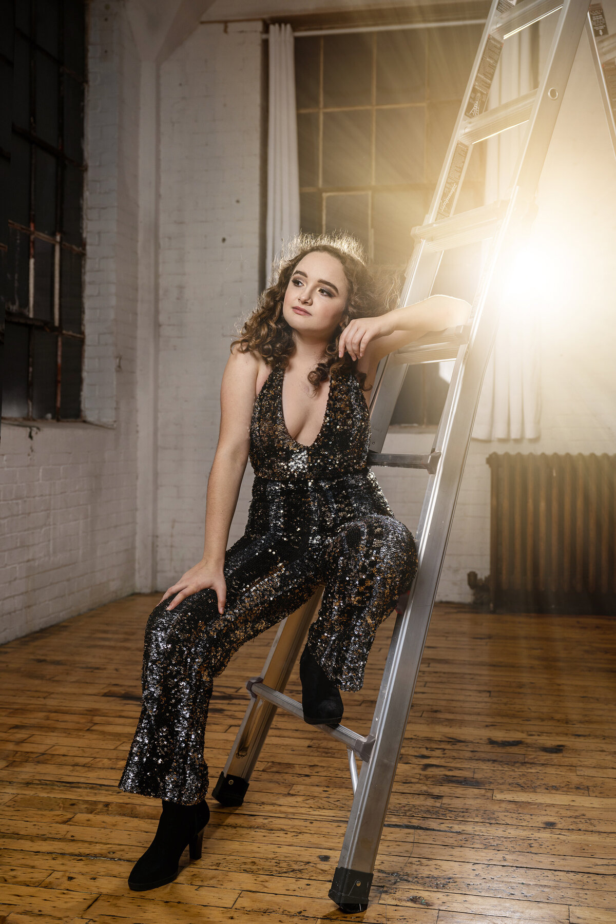 girl in sparkly jumpsuit sitting on ladder in a studio