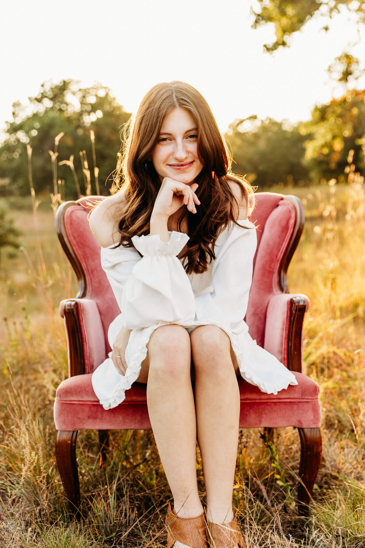 high school senior girl sitting in a pink velvet chair for her senior photo session