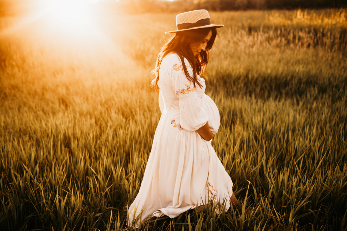 maternity session in a dress walking through a field at sunset
