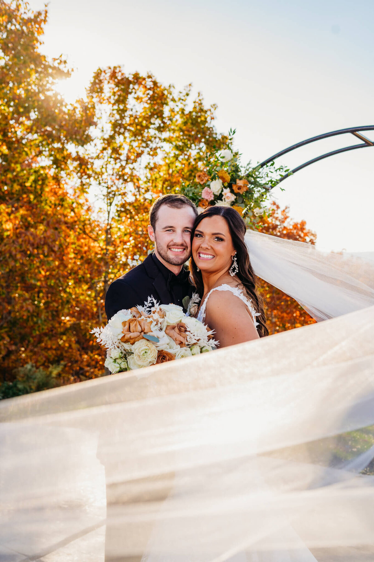 Photo of a bride and groom hugging and smiling while the brides veil flows in the wind