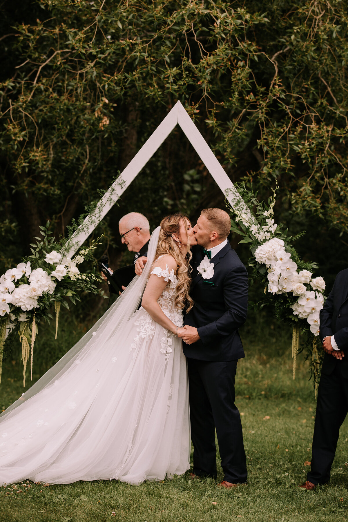 Triangle ceremony arch with classic and elegant white florals by Hen & Chicks, classic Calgary, Alberta wedding florist, featured on the Brontë Bride Vendor Guide.
