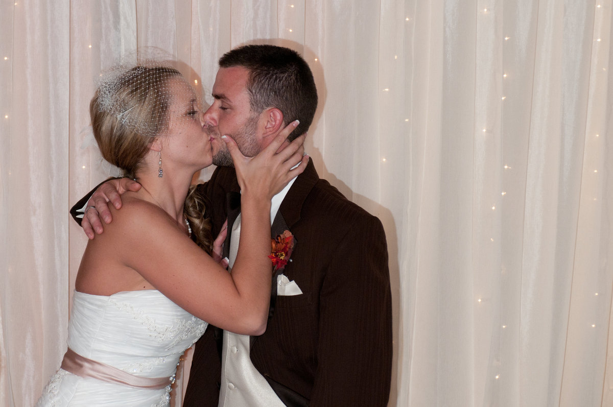 Bride and groom kiss in front of a white  curtain during the reception
