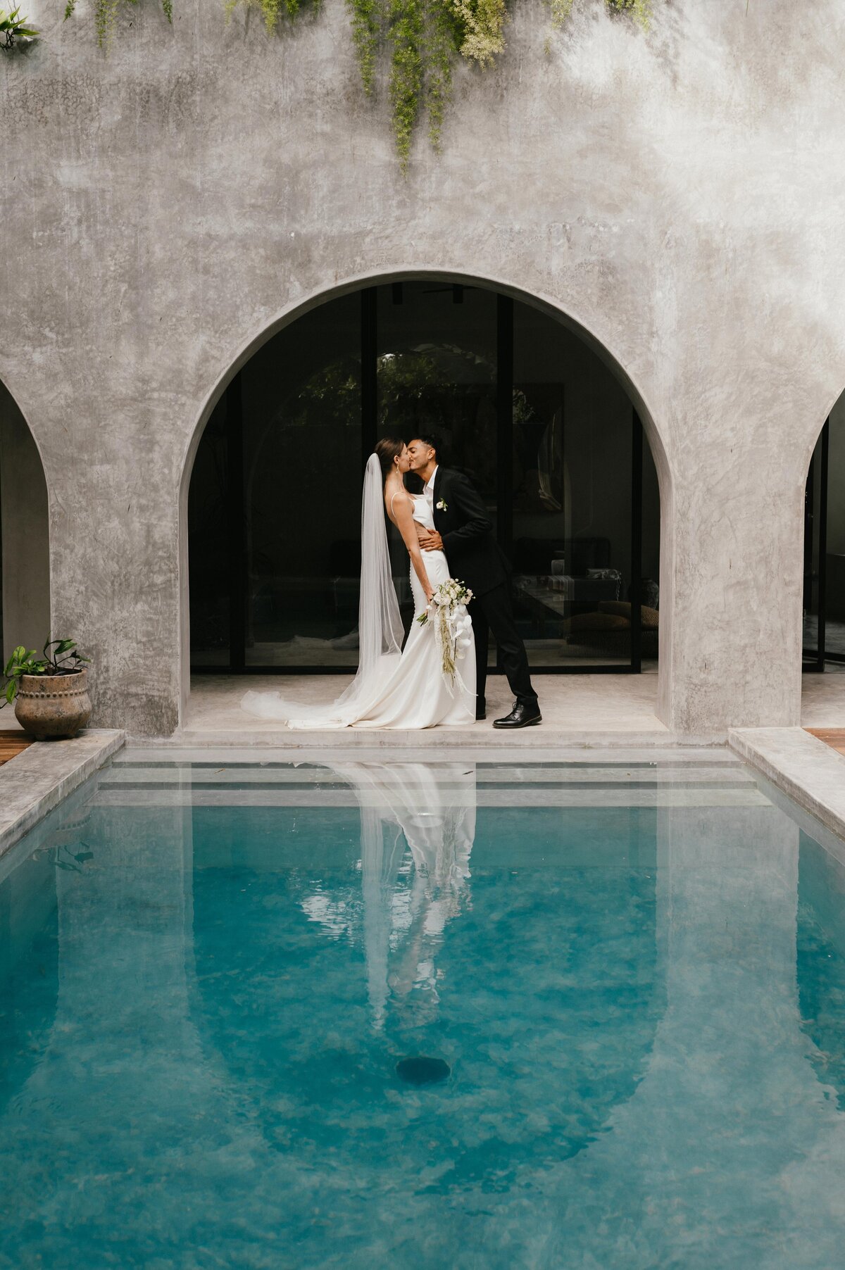 Wide angle of Greita and Jairo kissing in arch way at their Tulum villa elopement.