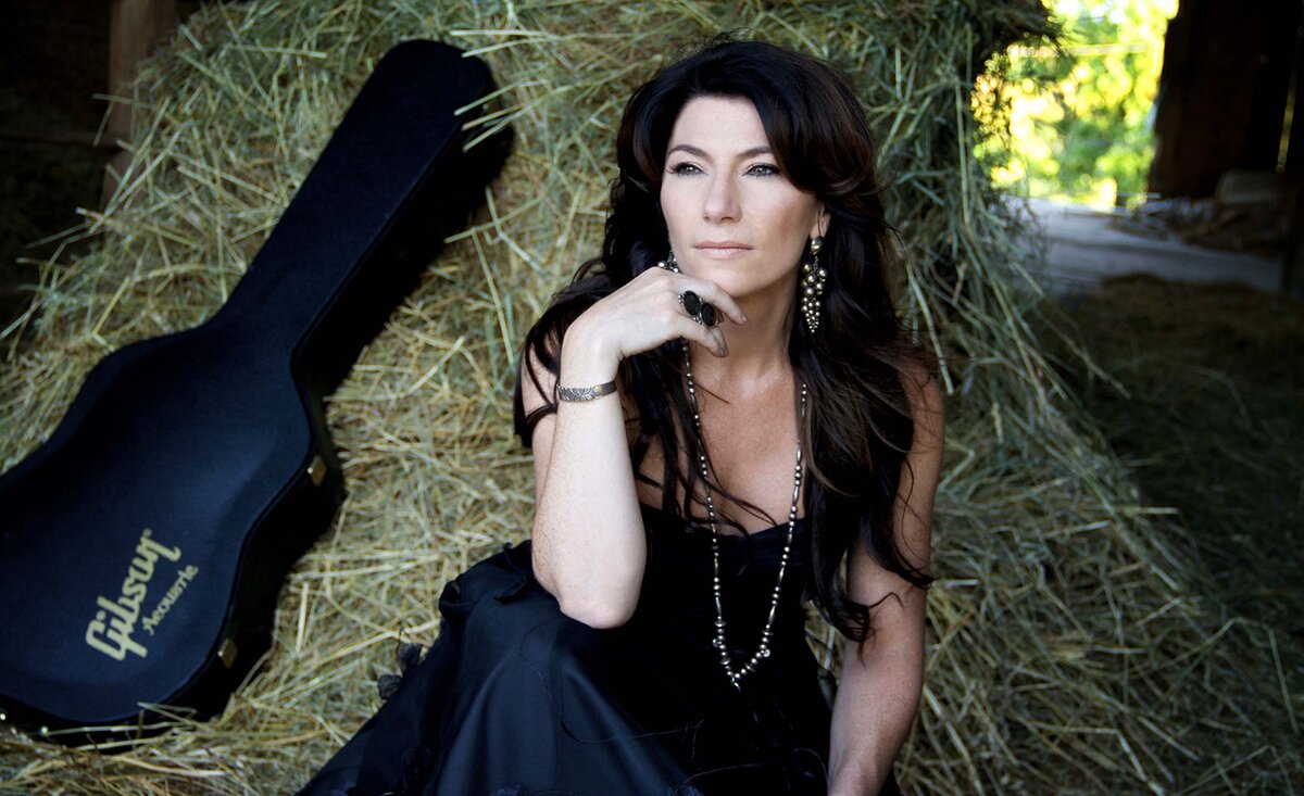 Country musician portrait Barbara Lynn Doran wearing black dress sitting against hay stack beside black guitar case