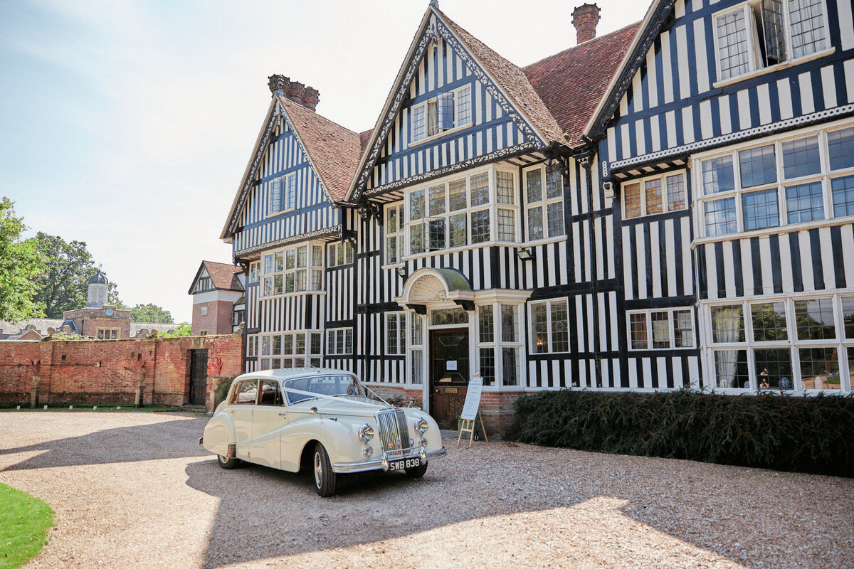 ivory vintage classic wedding car with silk ribbons on top parked by the brickwall wedding venue in rye east sussex