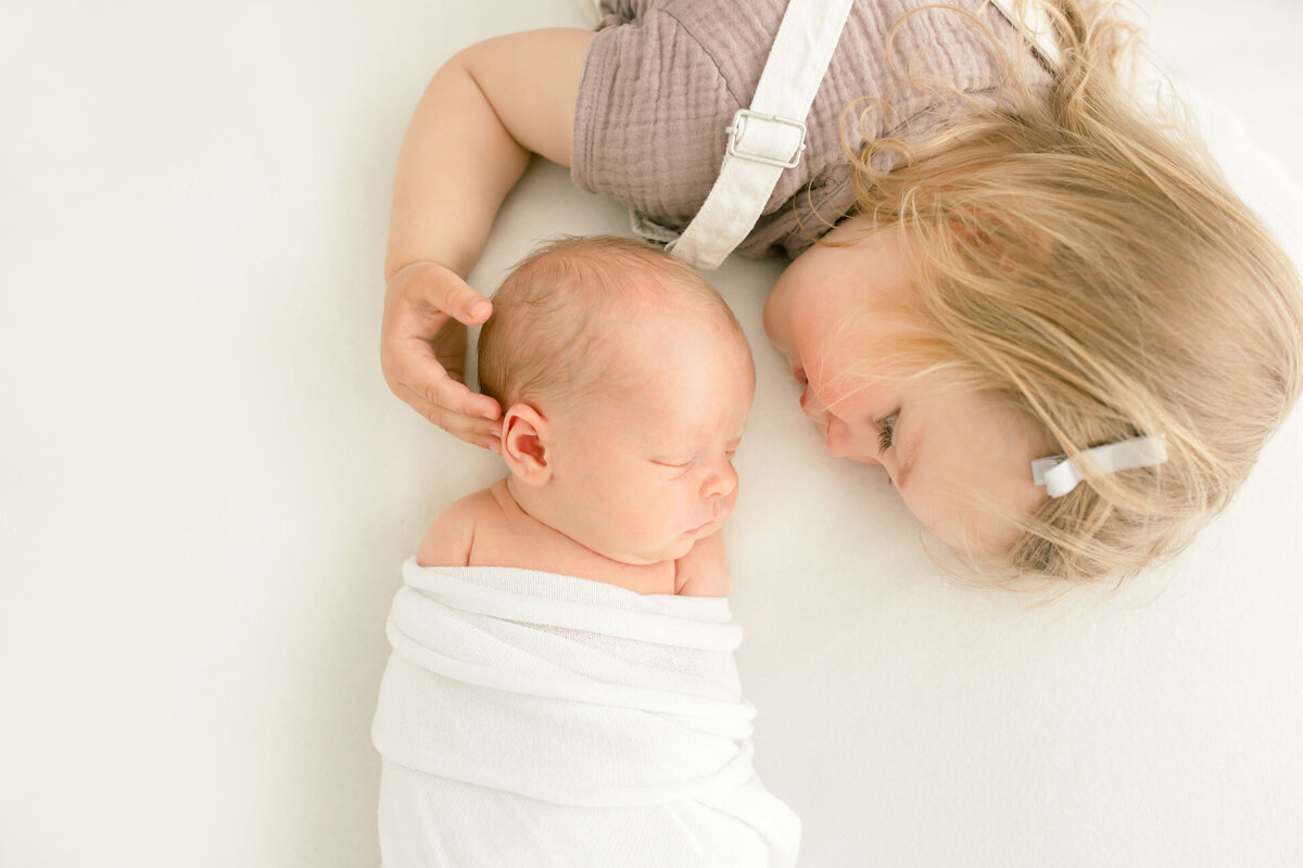 Geschwisterfotografie beim Babyfotoshooting: Baby in weiße Decke gewickelt mit Schwester