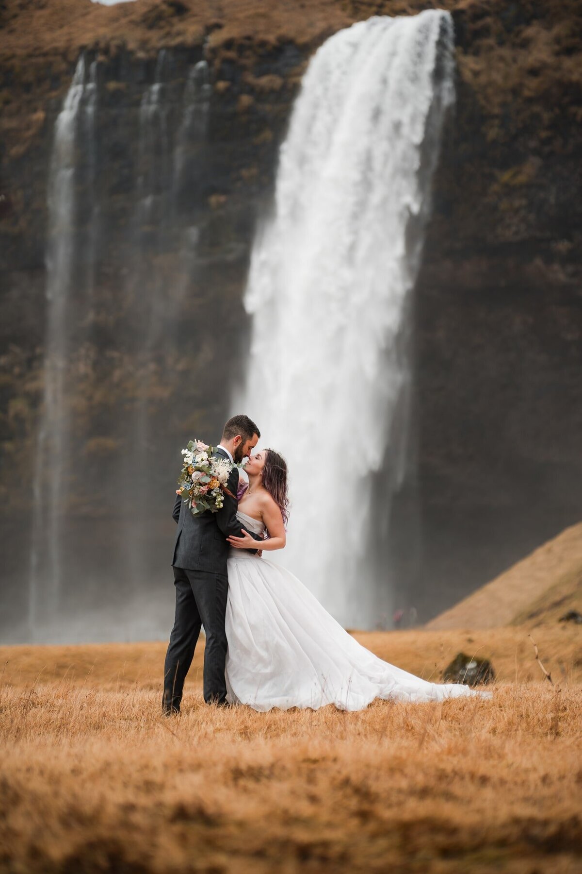 With a waterfall as their enchanting backdrop, this couple shares a nearly-kissing moment, capturing the magic of love amidst the beauty of Iceland.