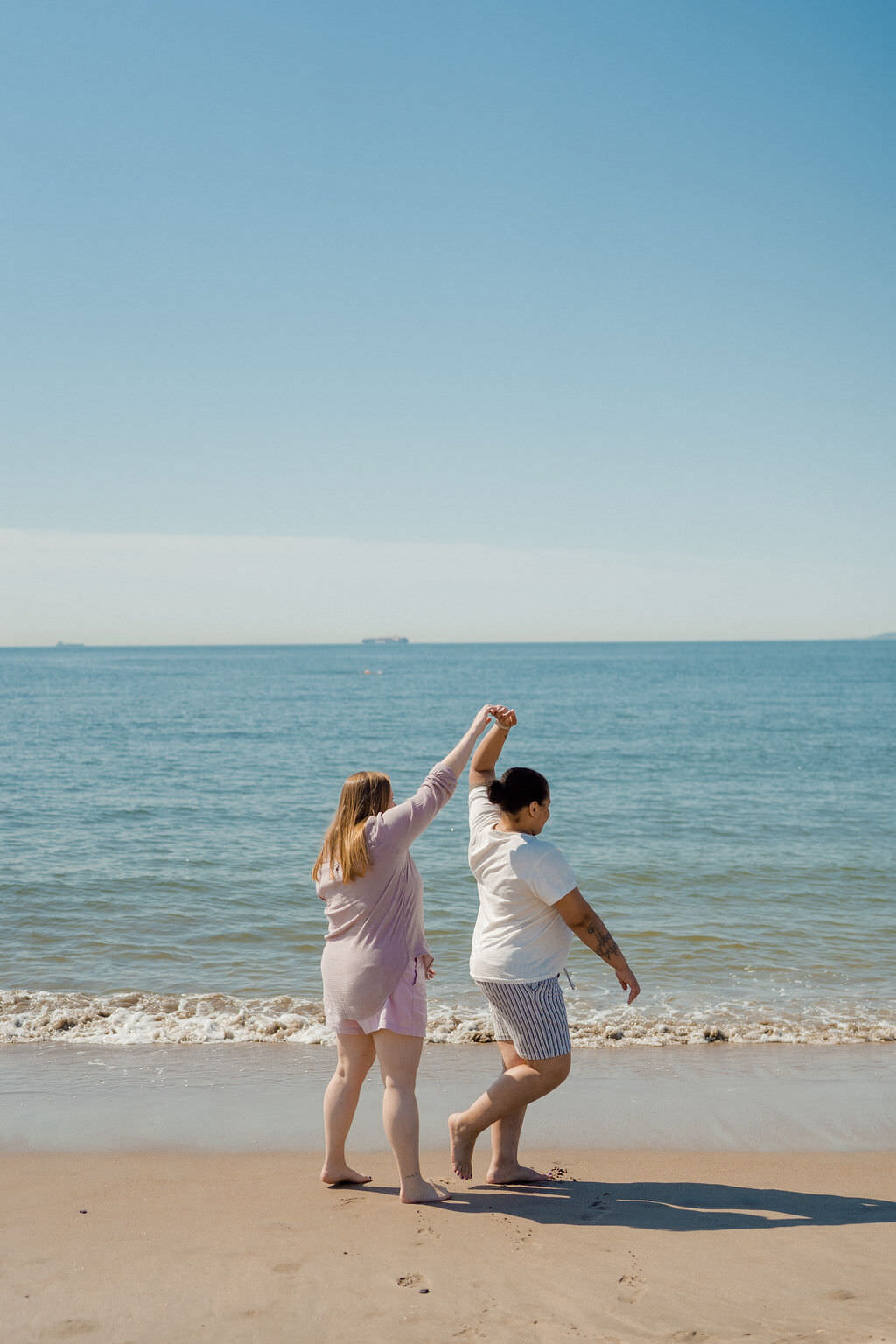woman with her arm up twirling her partner as they walk along the edge of the water