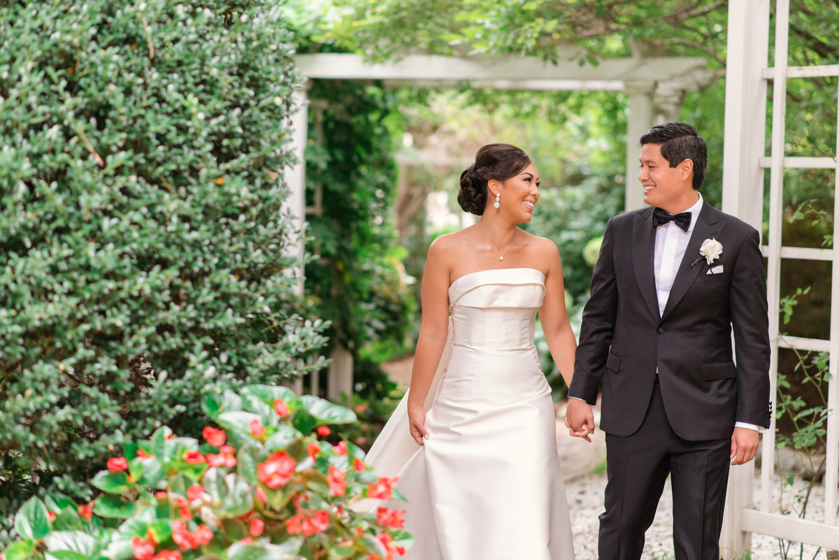 photo of bride and groom smiling and holding hands in the outdoor gardens from wedding reception at The Garden City Hotel