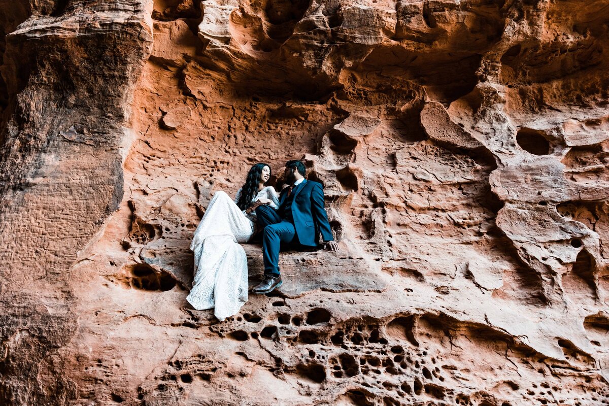 The bride and groom pose sitting on a cliff for their Utah elopement pictures