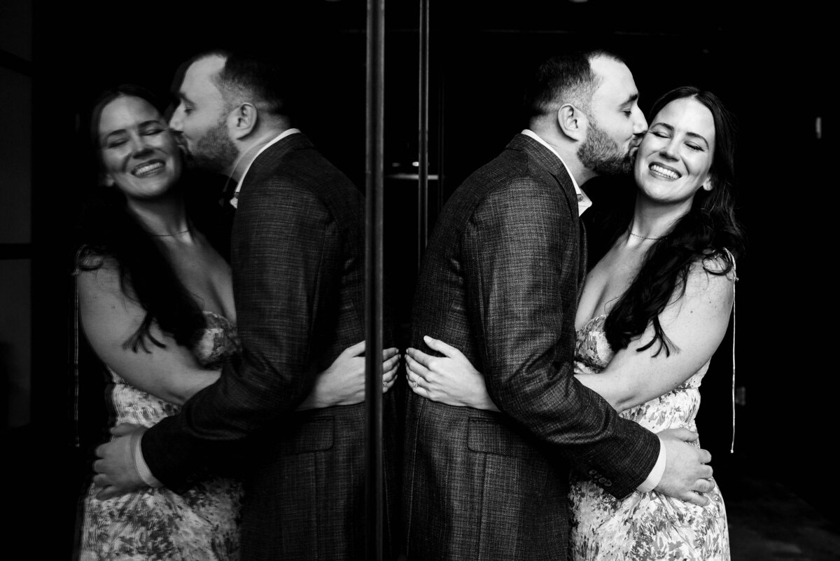 Black-and-white-reflection-image-of-engaged-couple-smiling-as-the-man-kisses-the-woman’s-cheek-at-Westside-Provisions-in-Atlanta