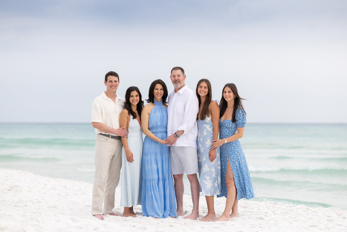 A family standing next to each other smiling along the water wearing blues and whites in Seaside Florida.