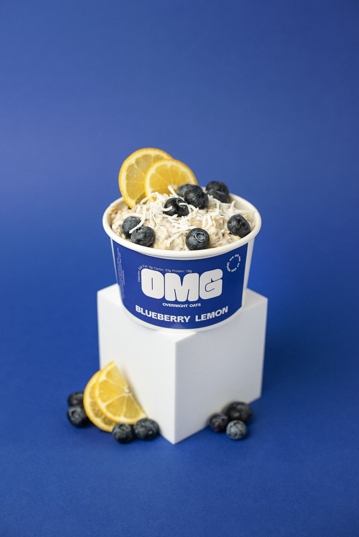Carton of oatmeal topped with blue berries and lemon sitting on a white block