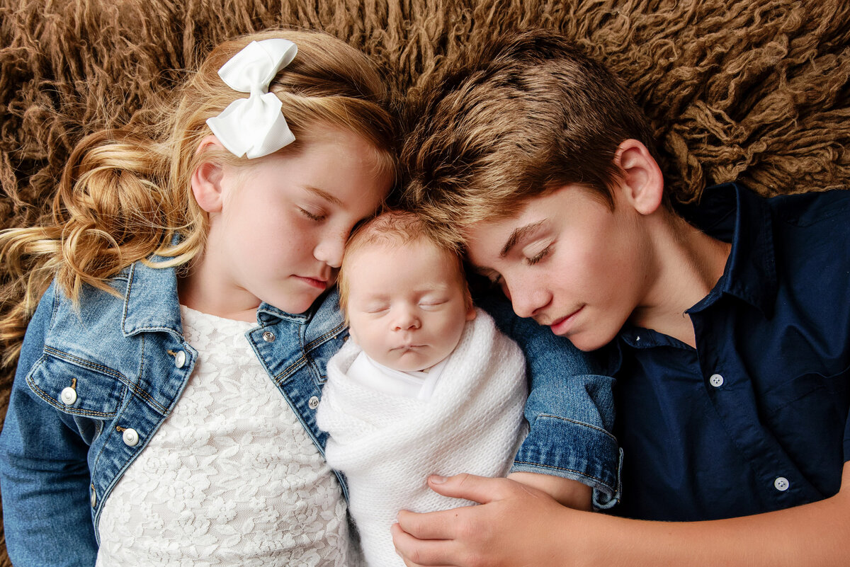 st-louis-newborn-photographer-siblings-snuggling-baby-in-blue-and-white-outfits-against-brown-shag-background