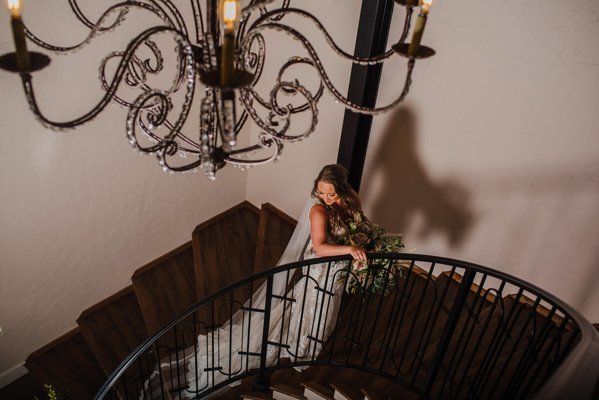 Photo of a bride as she walks up a stairwell with a chandelier overhead