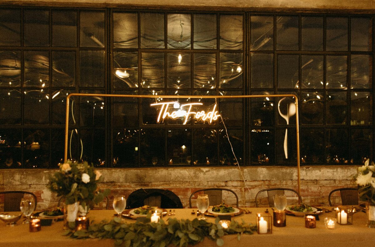 Dimly lit wedding reception venue in Iowa with "the frosts" in neon writing on a window, a decorated table with candles and flowers in the foreground.