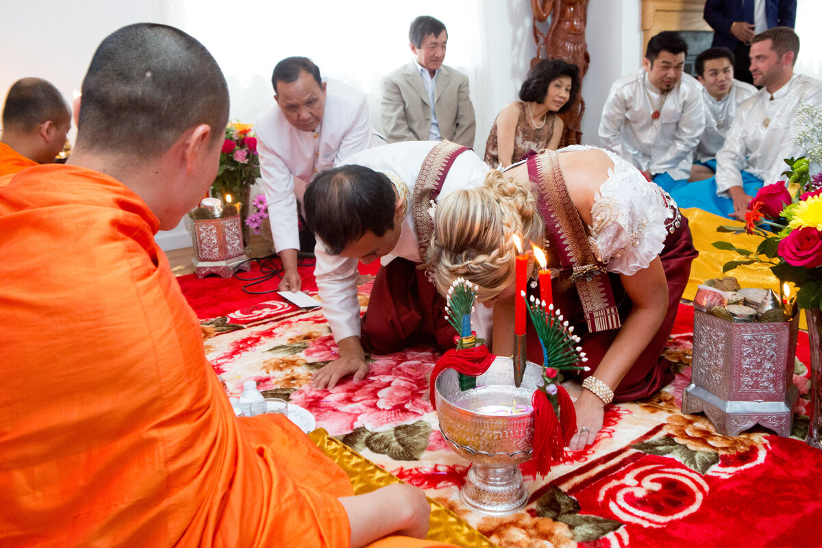 Buddhist bride and groom kneel before a monk in saffron robes New York wedding photographer Milestone Images