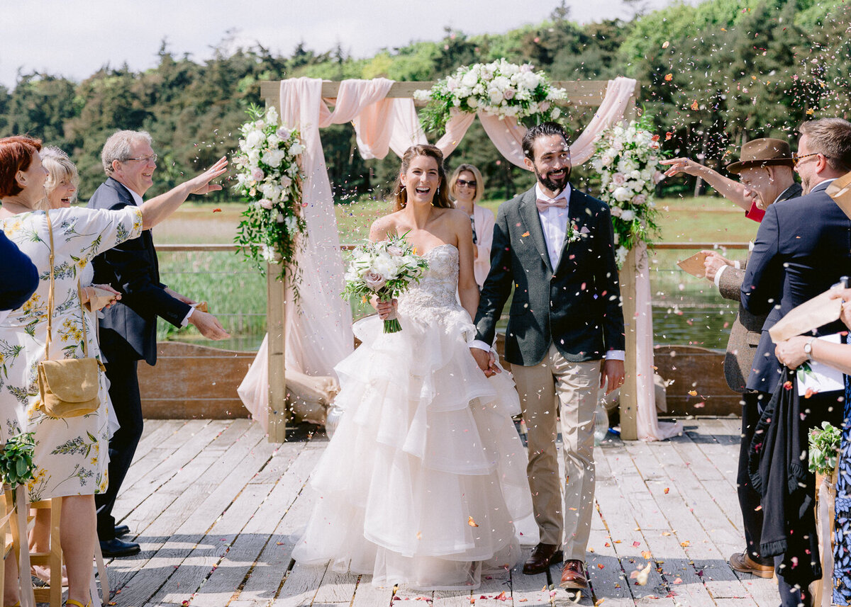bride and groom walking down the aisle while guests throwing fresh flower petals