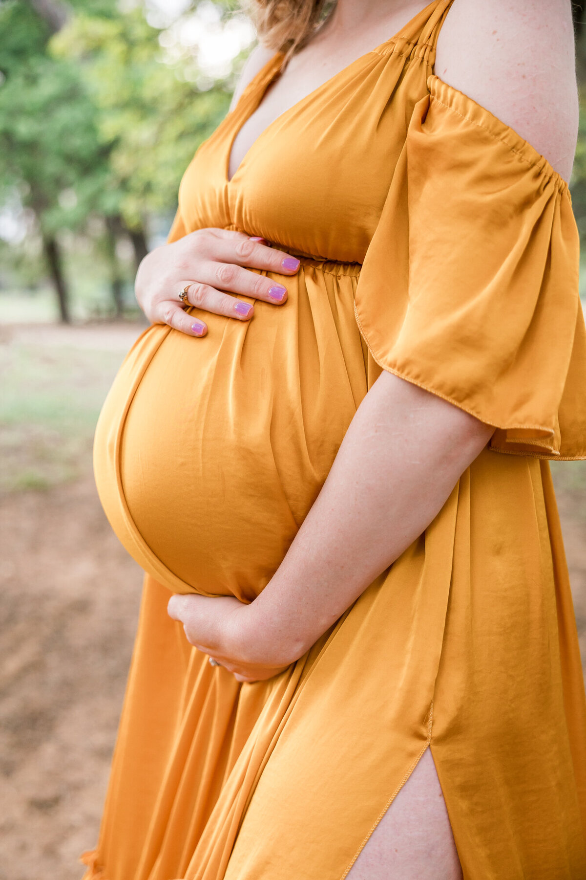 woman holds her belly while wearing a yellow colored maternity gown