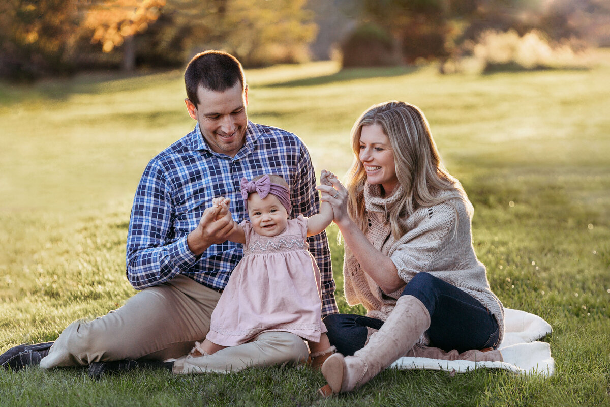 mom and dad sitting on a blanket with their toddler daughter at sunset at an outdoor family session