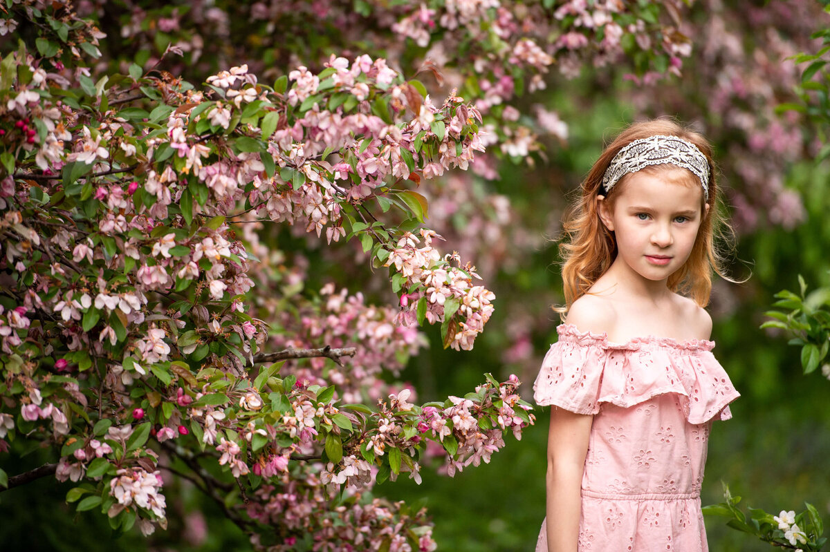 a little girl with red hair and pink dress smiles shyly during family photography in Ottawa's Arboretum