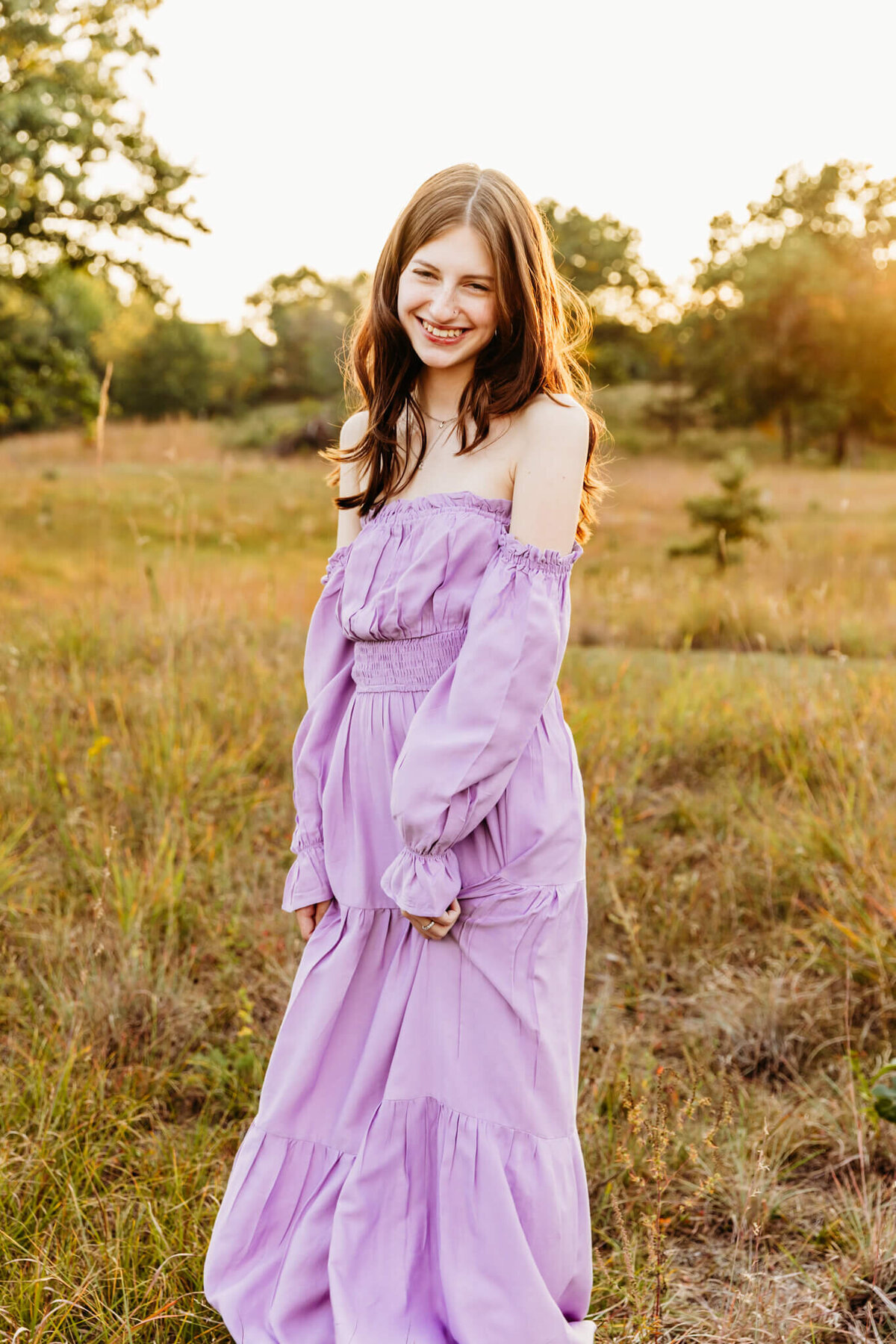 teen girl in a purple dress smiling while holding dress in a field near Appleton WI