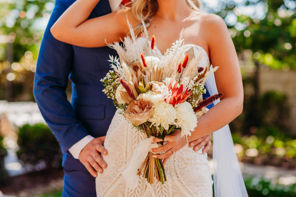 photo of a bride's bouquet while the bride and groom are cuddling in the background