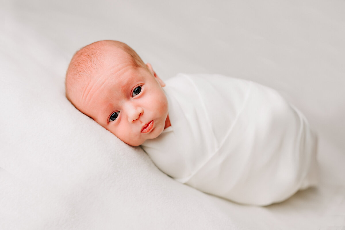 baby girl swaddled in white on a white blanket.