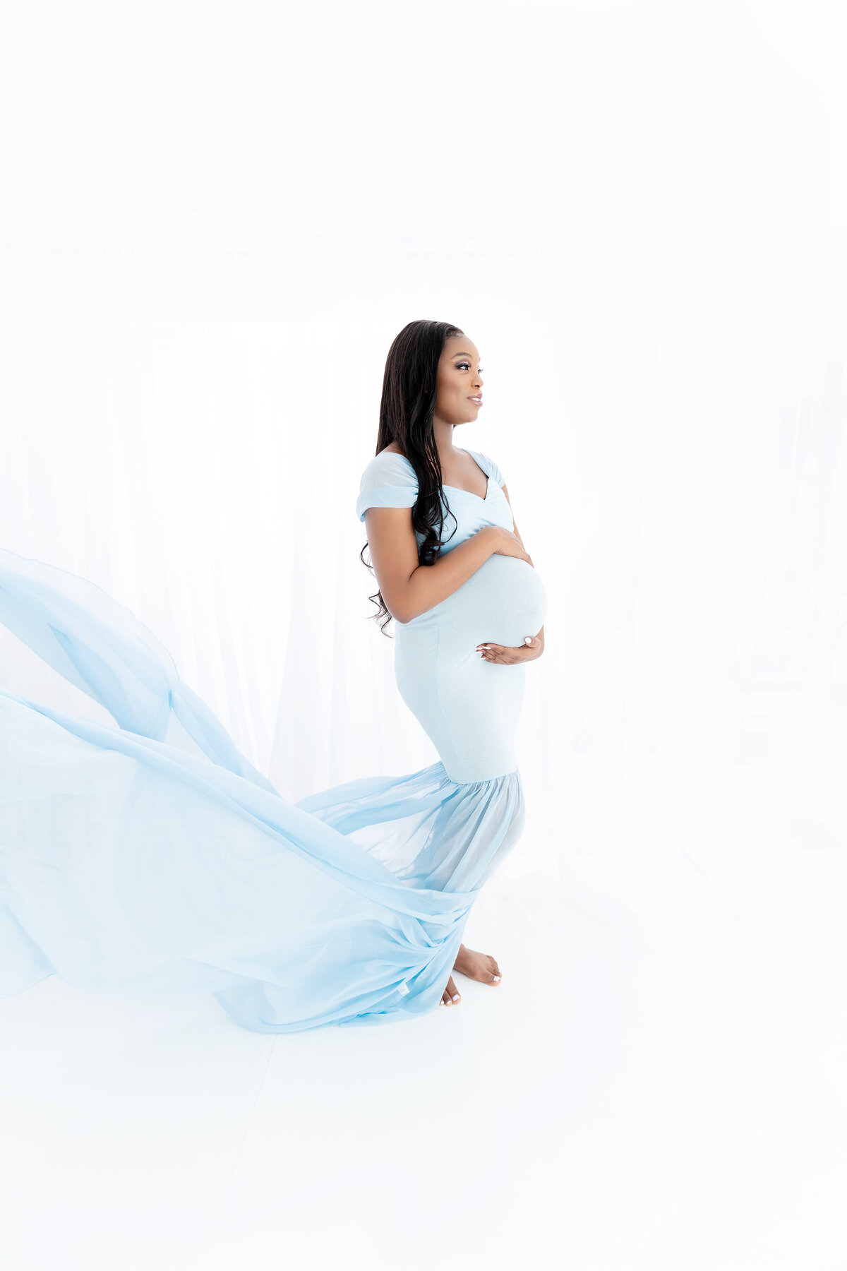 A woman in a flowing maternity gown stands in a studio holding her bumpAtlanta Maternity Photographer