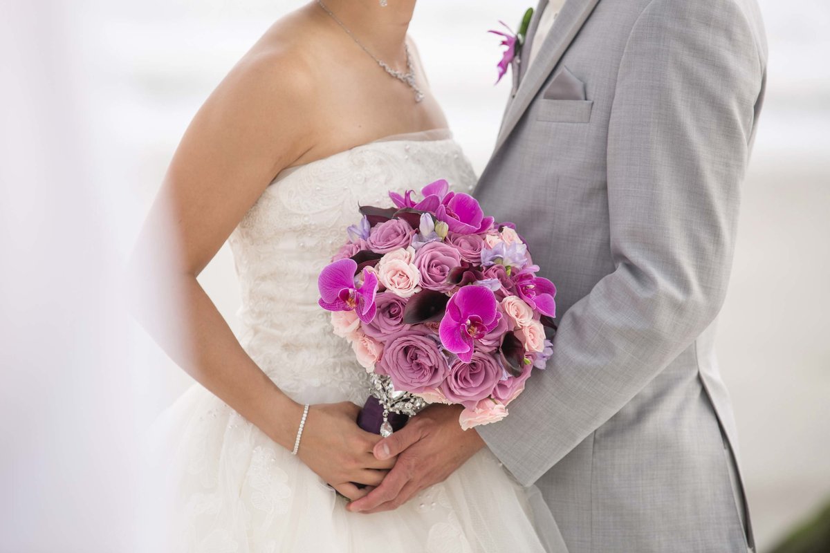 Bride and groom holding a bouquet of pink and purple flowers at Bridgeview Yacht Club