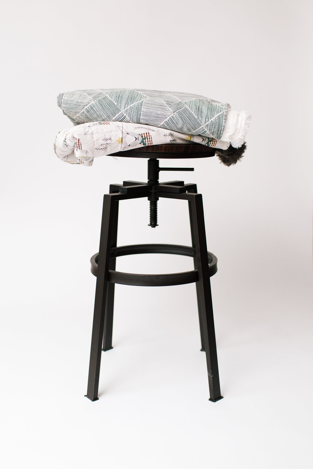 blankets stacked on black stool on white background