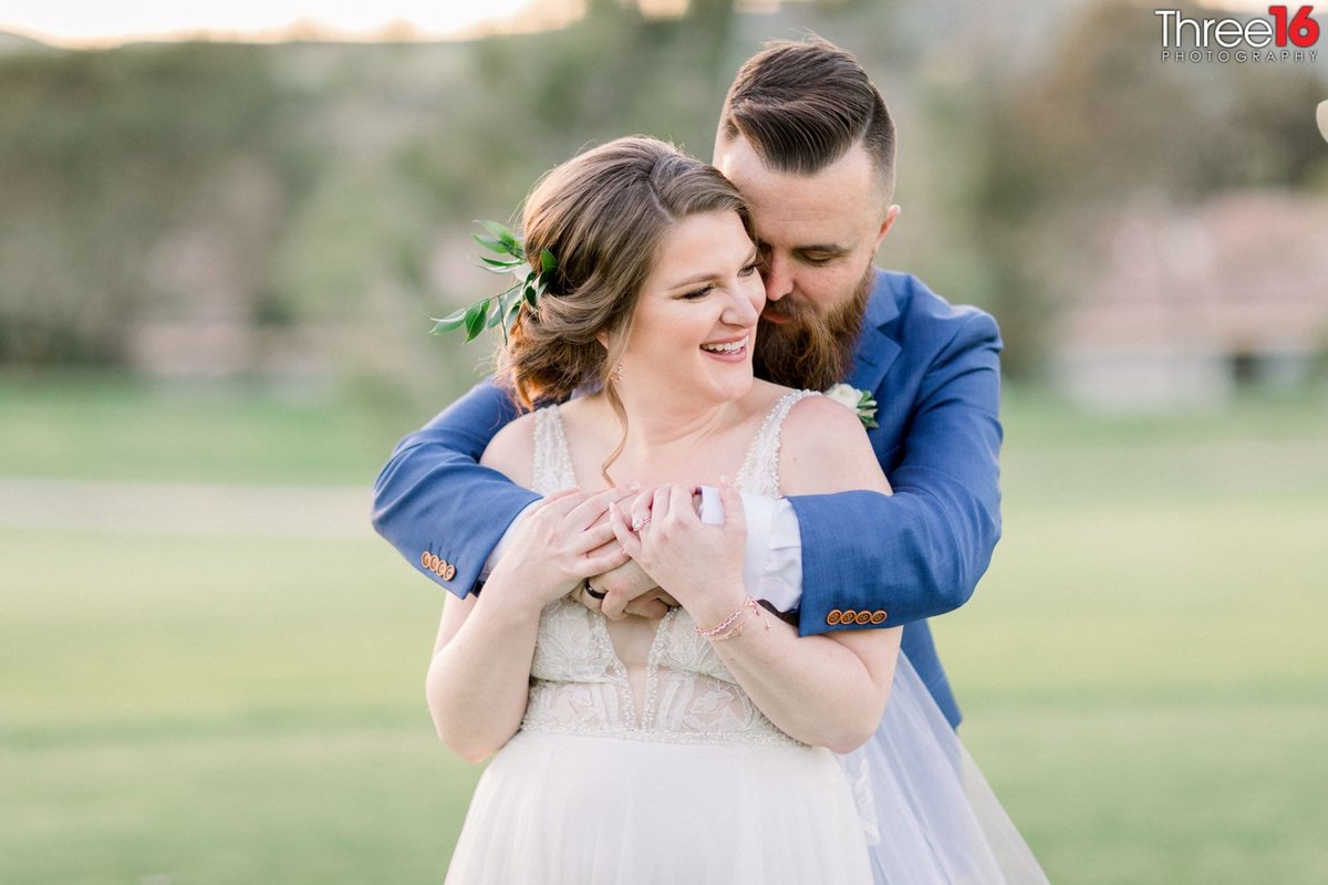 Groom embraces his Bride from behind and whispers causing her to laugh