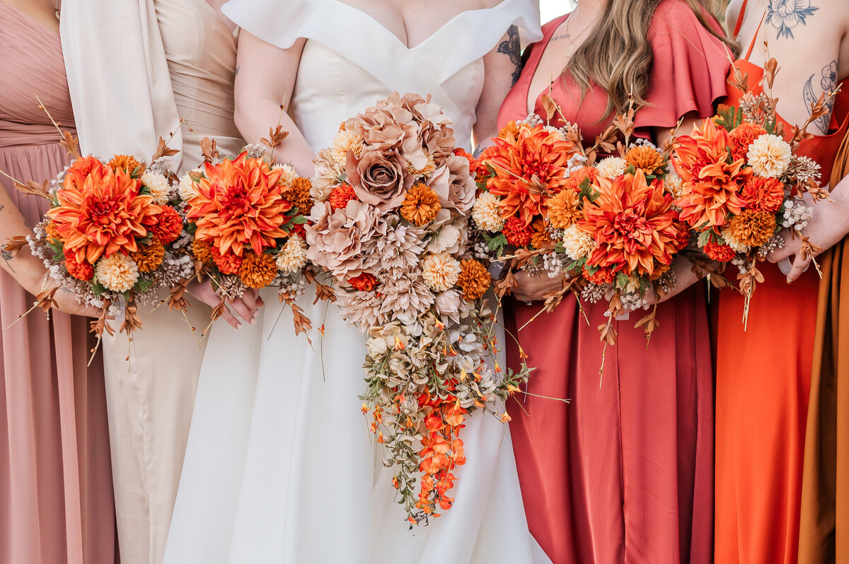 A bride holding orange flowers next to her bridesmaids in orange dresses by JoLynn Photography, a Raleigh wedding photographer