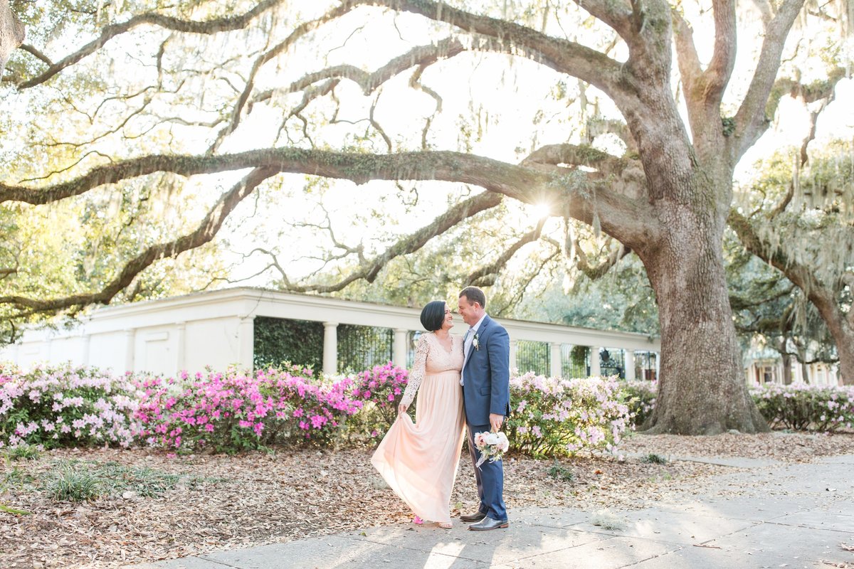 bride ang groom standing under an oak tree with azaleas blooming in forsyth park savannah