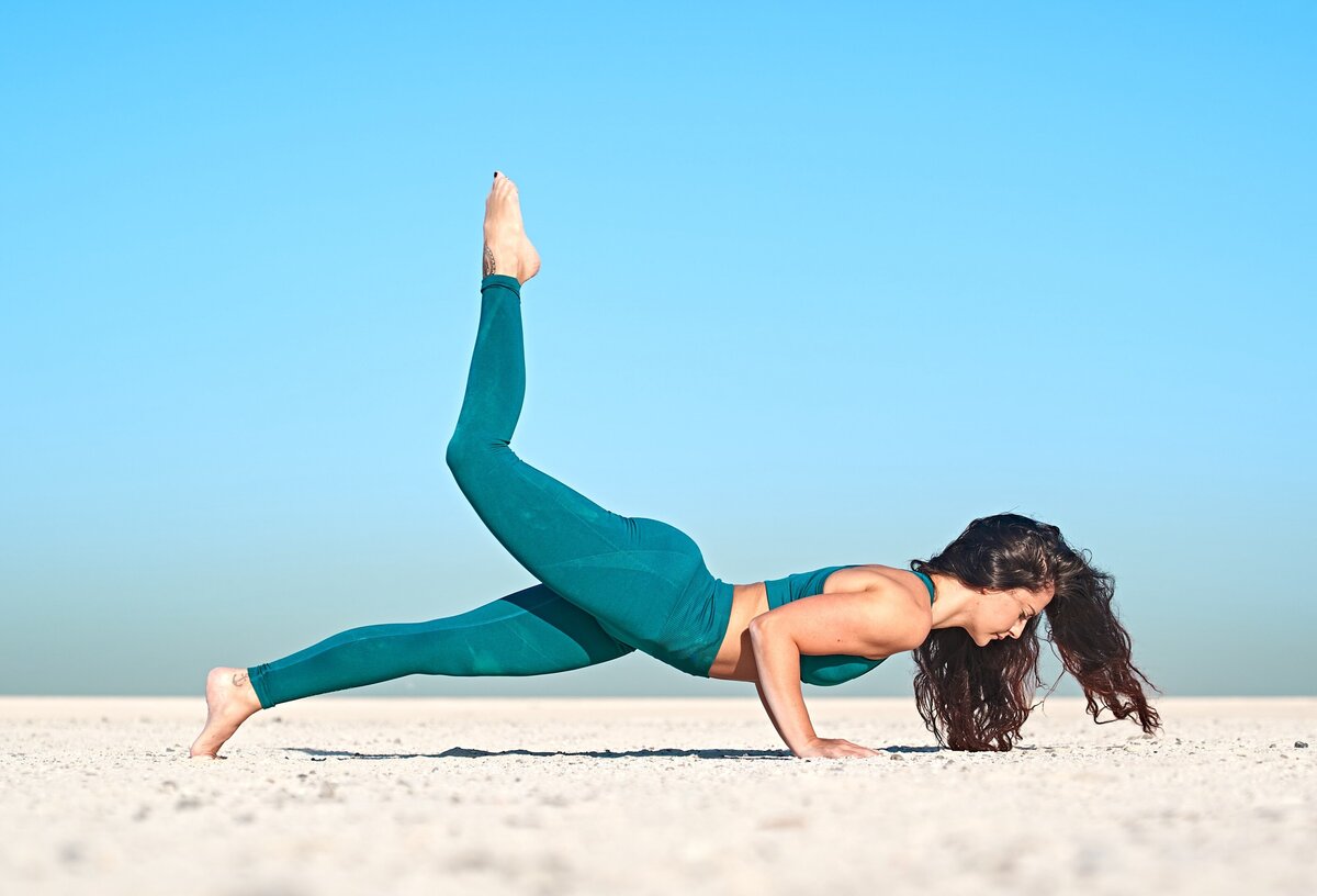 Sarah exhibits a powerful one-legged push-up pose, poised against the clear desert sky, showcasing strength and flexibility integral to advanced yoga practice.