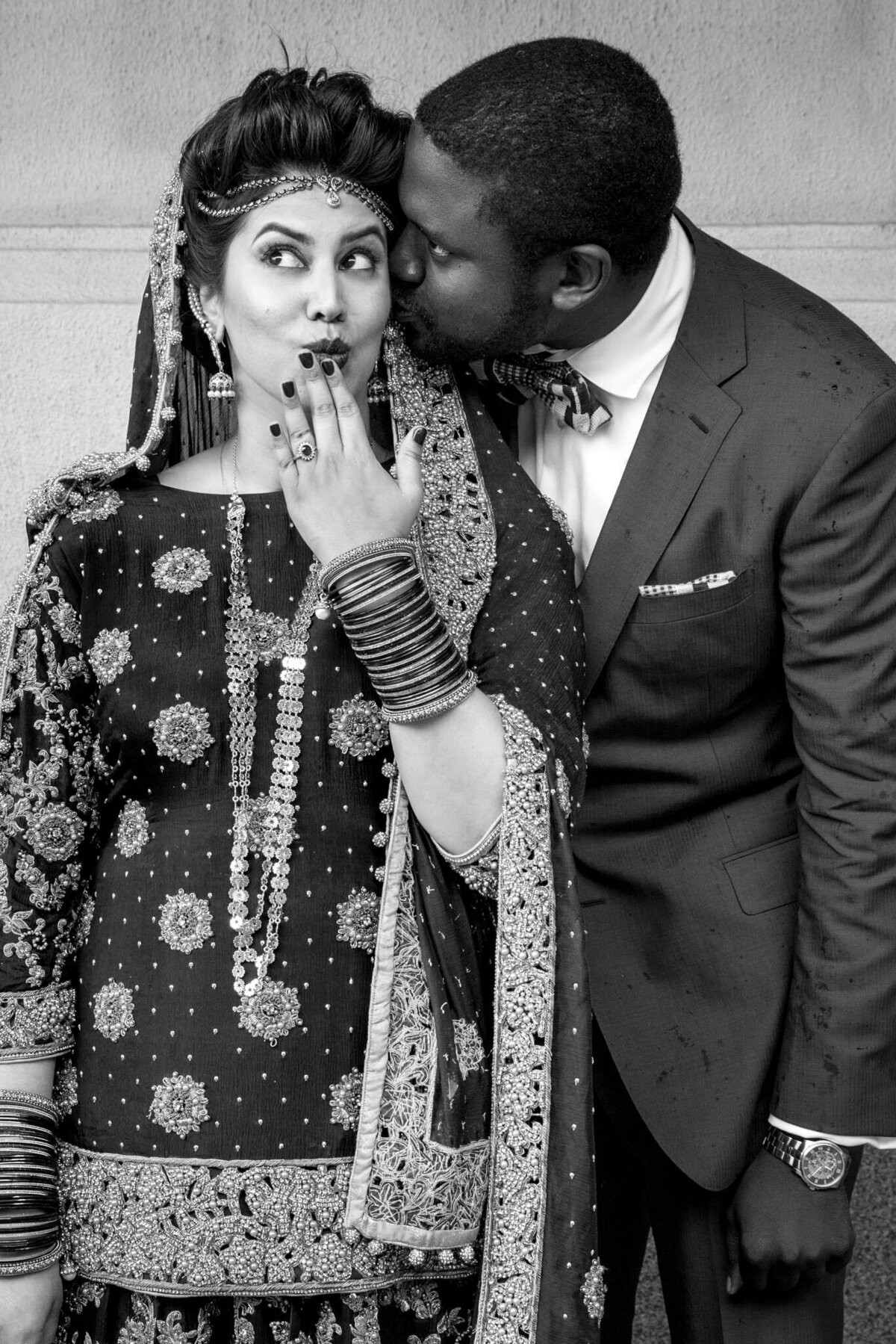A black and white photo of a groom kissing his partner's cheek.