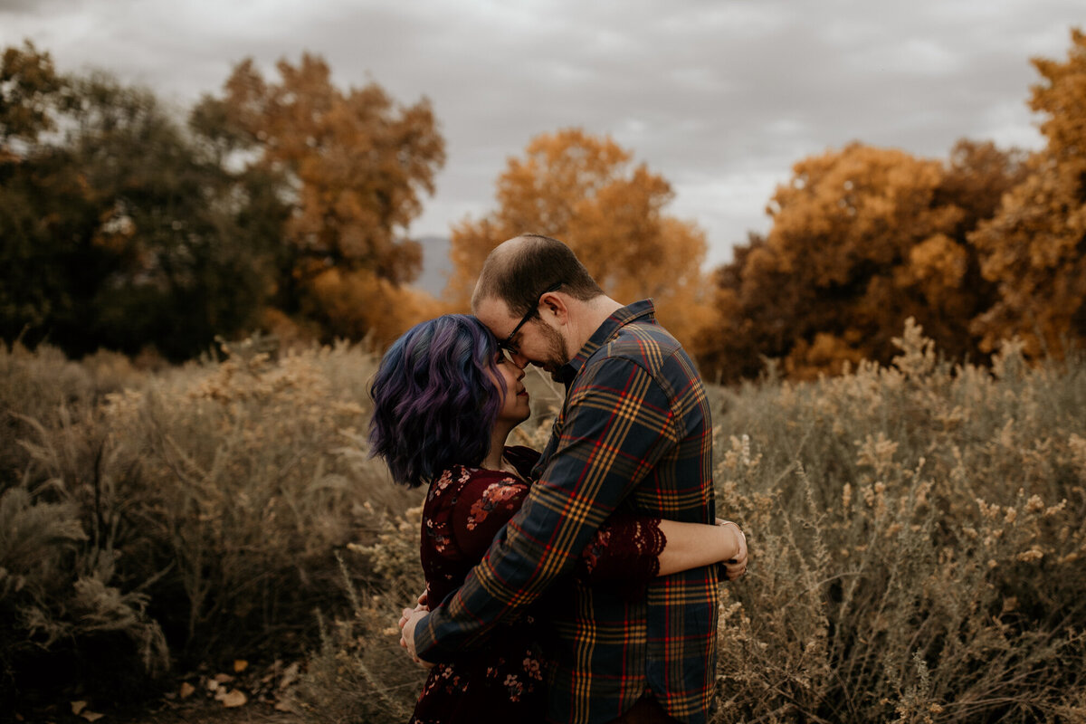 blue haired wife holding husband with fall leaves behind them