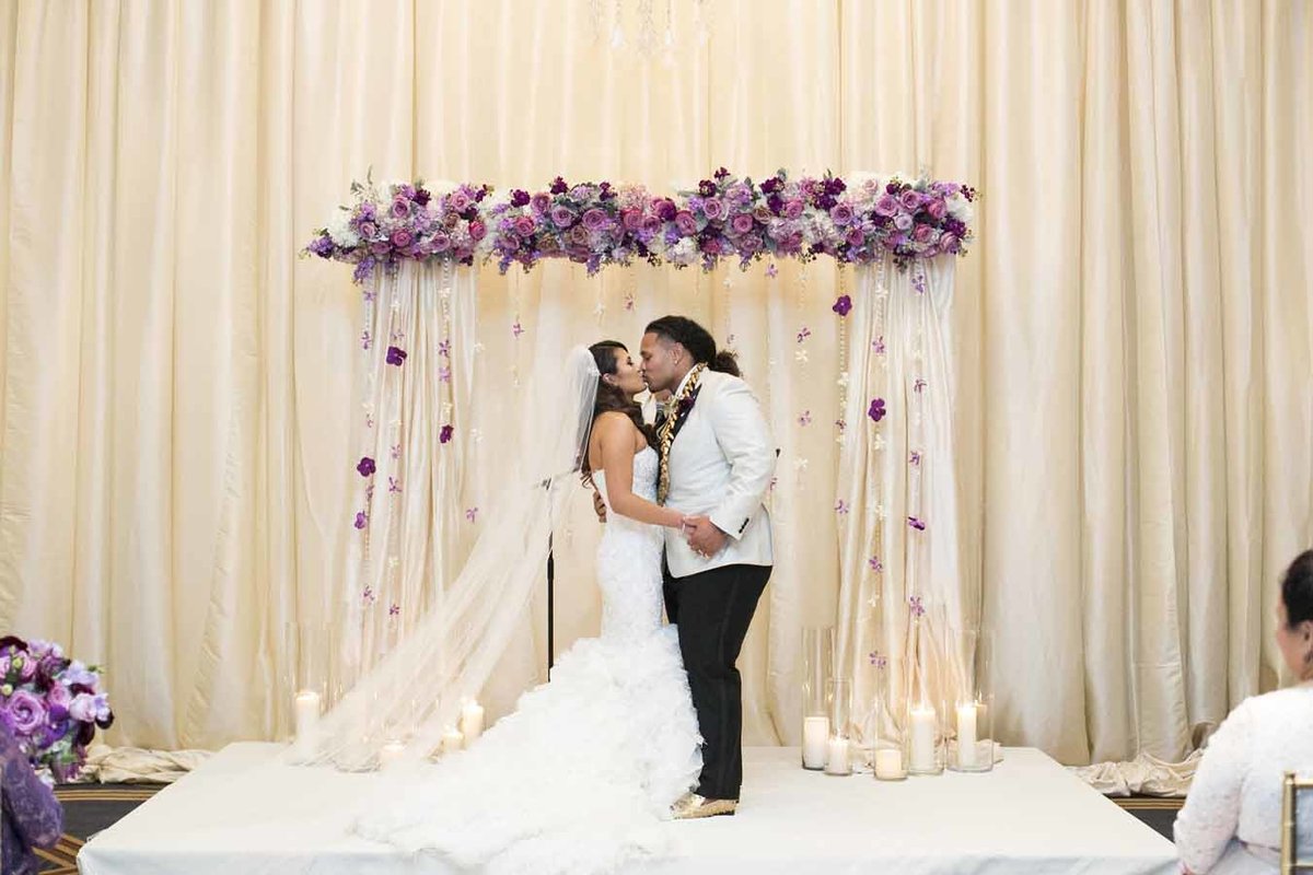 Beautiful ceremony arch with dangling strands of crystal and orchids frame the couple.