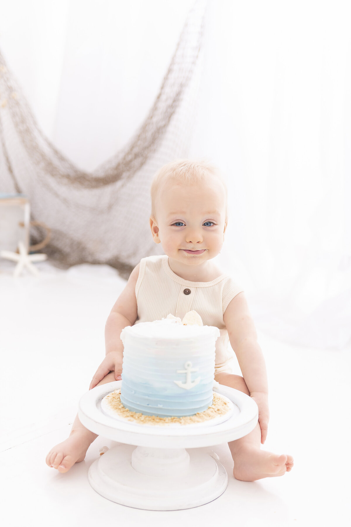A happy toddler sits in a studio behind a nautical themed cake