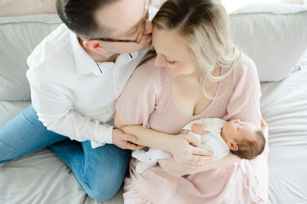 husband kissing is wife's forehead while holding baby