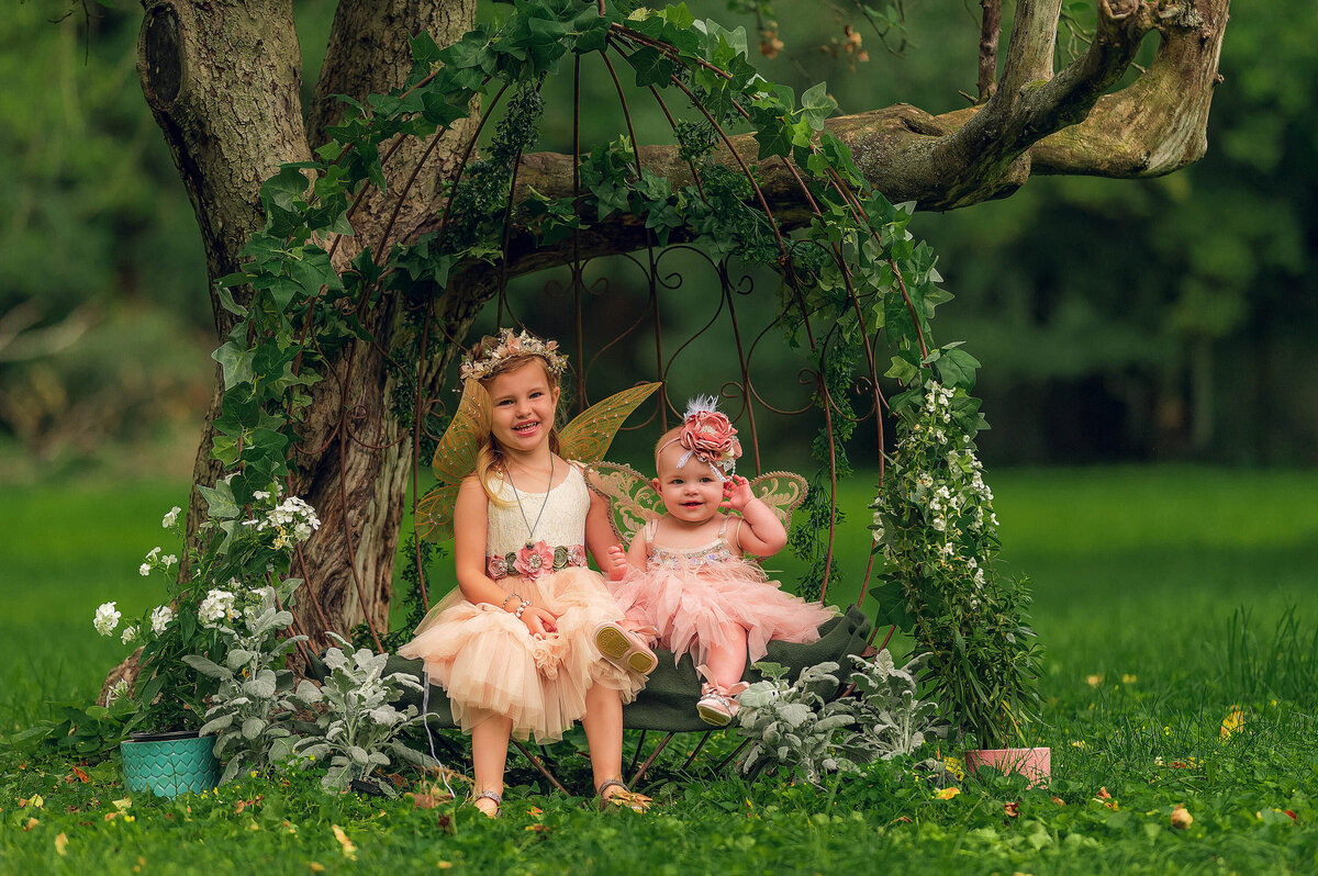 A young girl and her baby sister sit for a whimisical fairy portrait session in their Hartland, WI yard.
