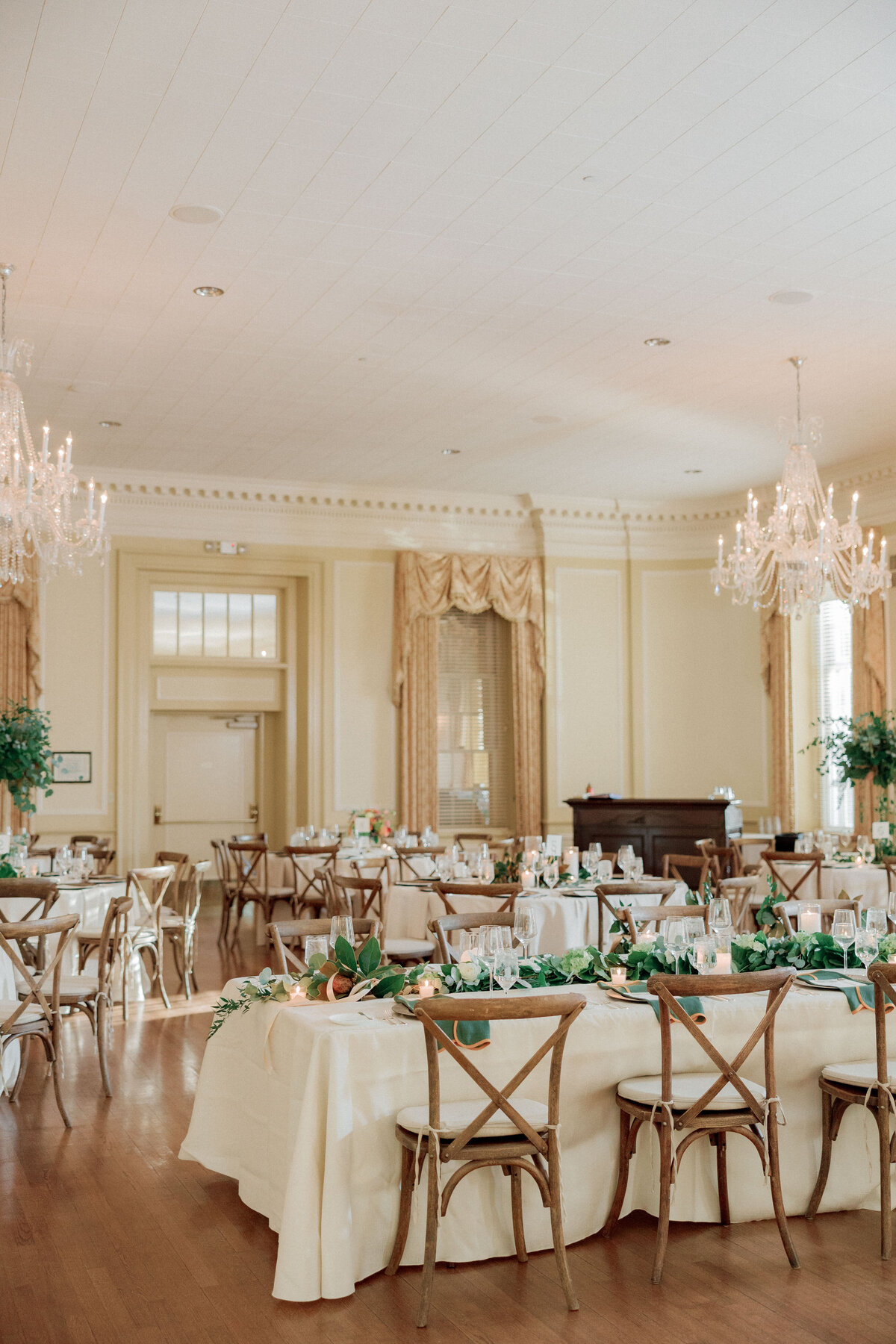Indoor wedding reception with neutral linens,  wood chairs, and simple greenery tablescape