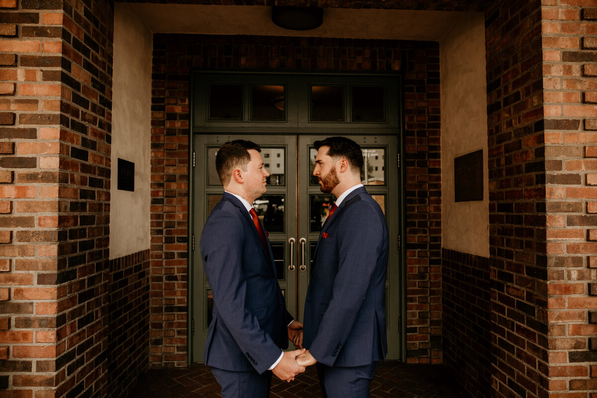 same sex couple standing in front of a brick building in downtown Albuquerque holding hands