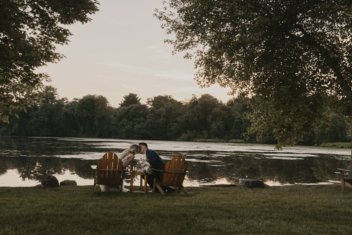 Groom and bride in adirondack chairs near a lake