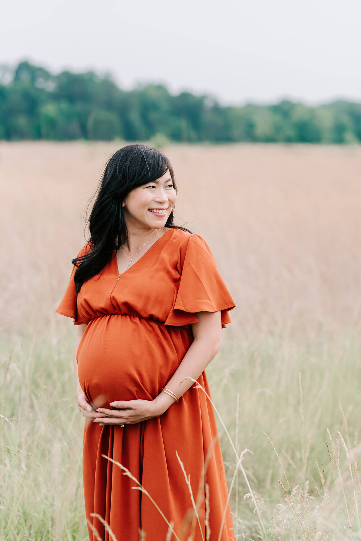 A woman in orange smiling at her partner and dog during her maternity shoot by a northern virginia maternity photographer