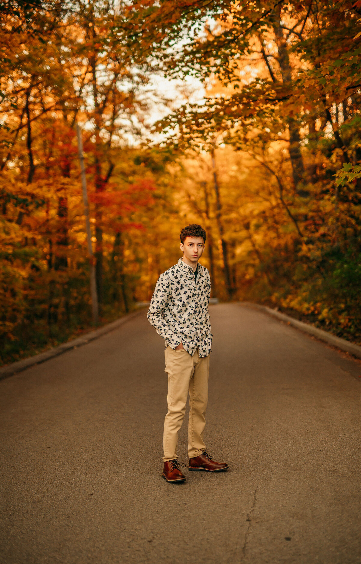 A New Berlin West High School student stands in the middle of a Delafield road  lined with trees in full autumn color for his senior portraits.