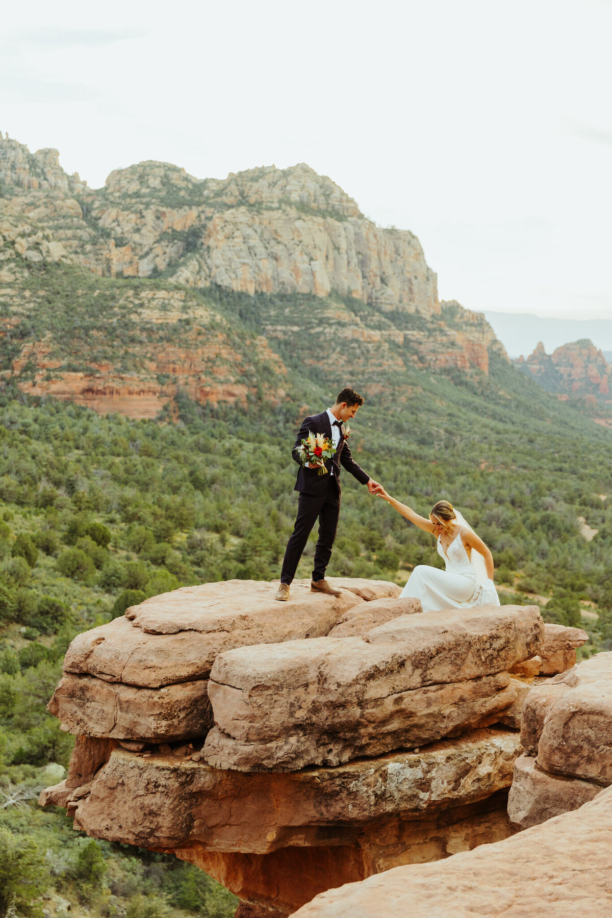 man helps woman get the to top of a rock at merry go round rock in sedona