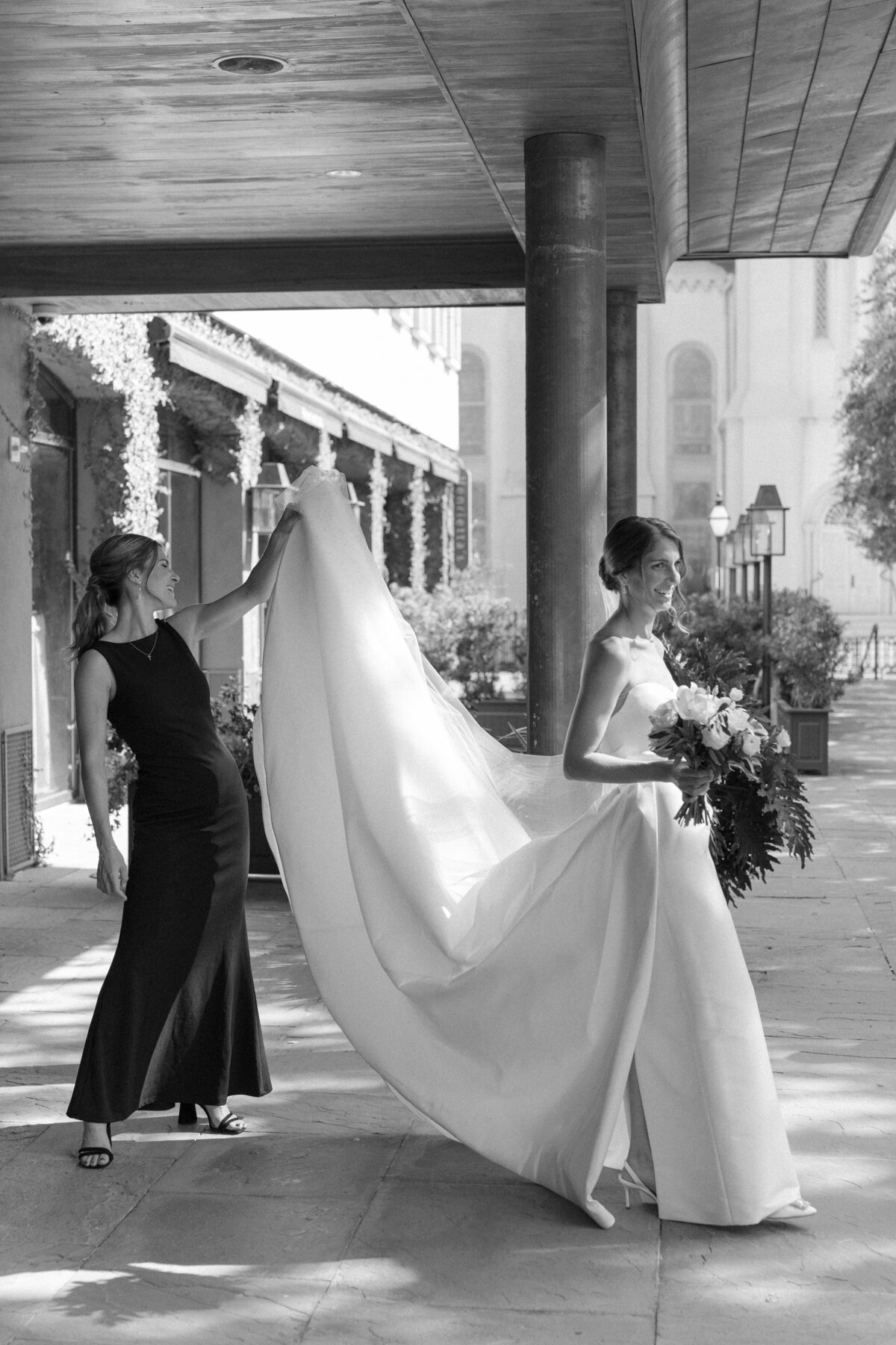 Candid black and white photo at the Dewberry Hotel in downtown Charleston. Maid of honor helps bride keep her wedding dress clean. Documentary style wedding photographer. Kailee DiMeglio Photography.